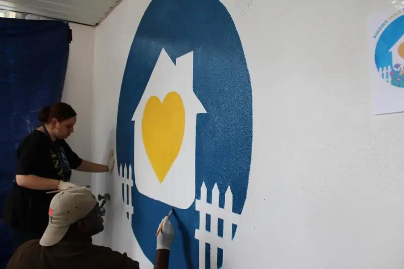 Community members paint a heart and house mural together.