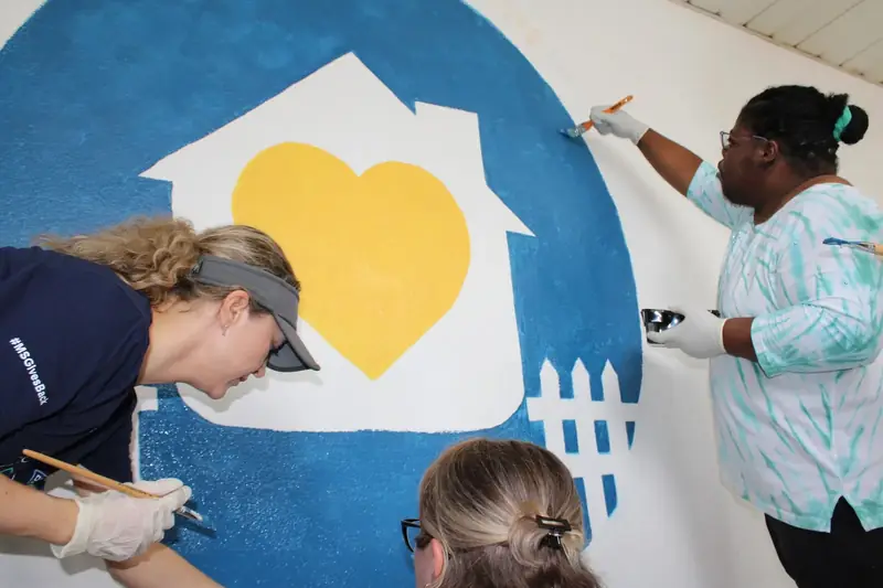 Volunteers paint the blue and yellow Friendship House community mural.