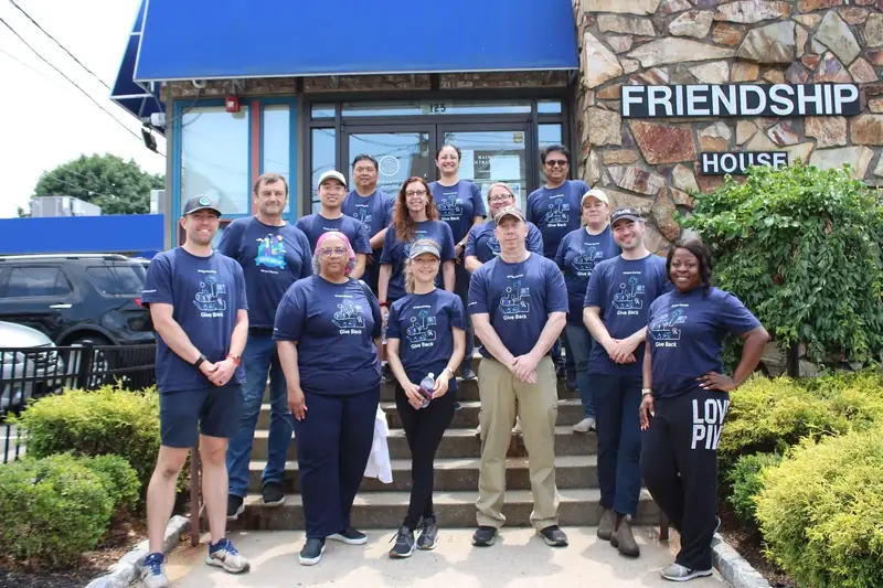 A volunteer group poses together outside the Friendship House entrance.